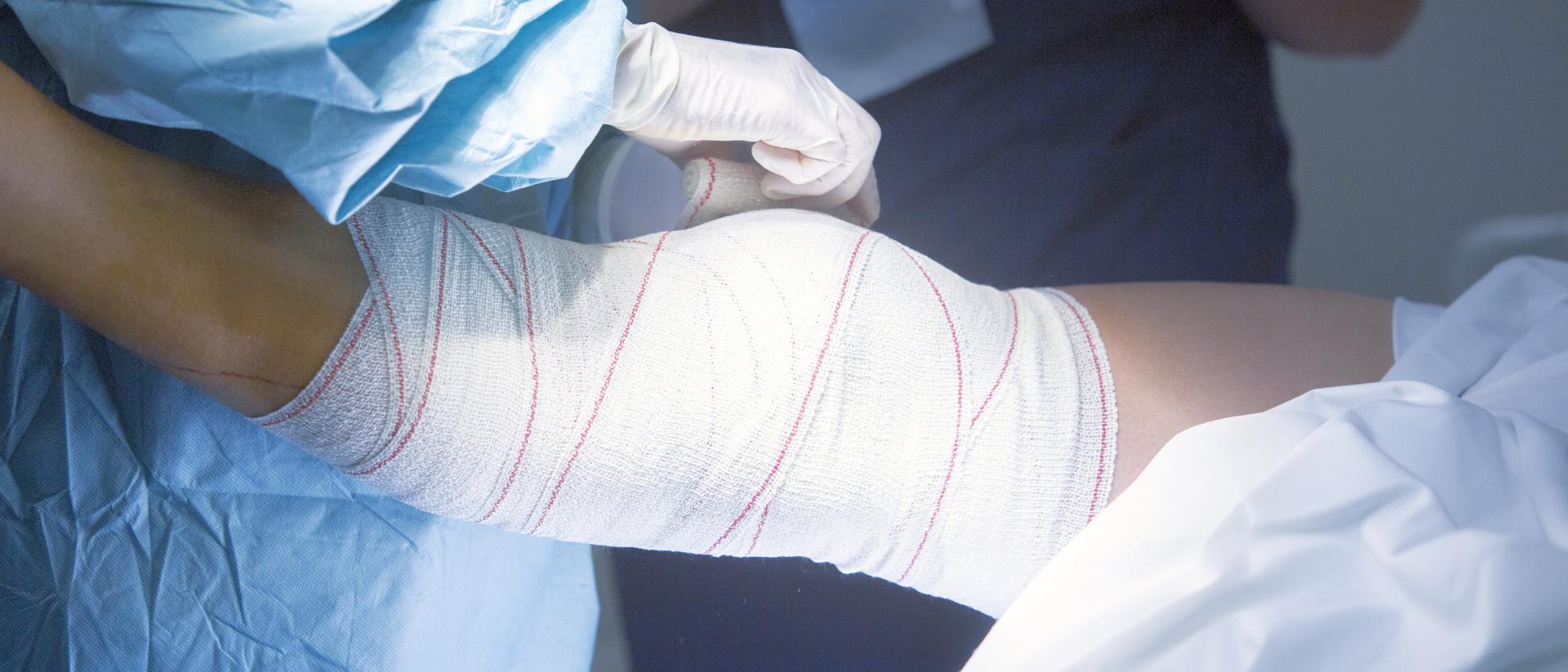 Ein Patient bekommt seine Wunde am Knie mit einem Verband verbunden.